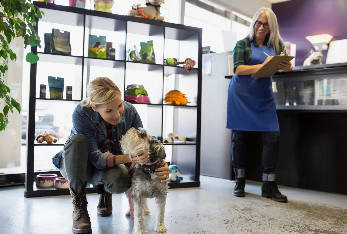 Woman staff member greeting small tan dog at Dog House facility