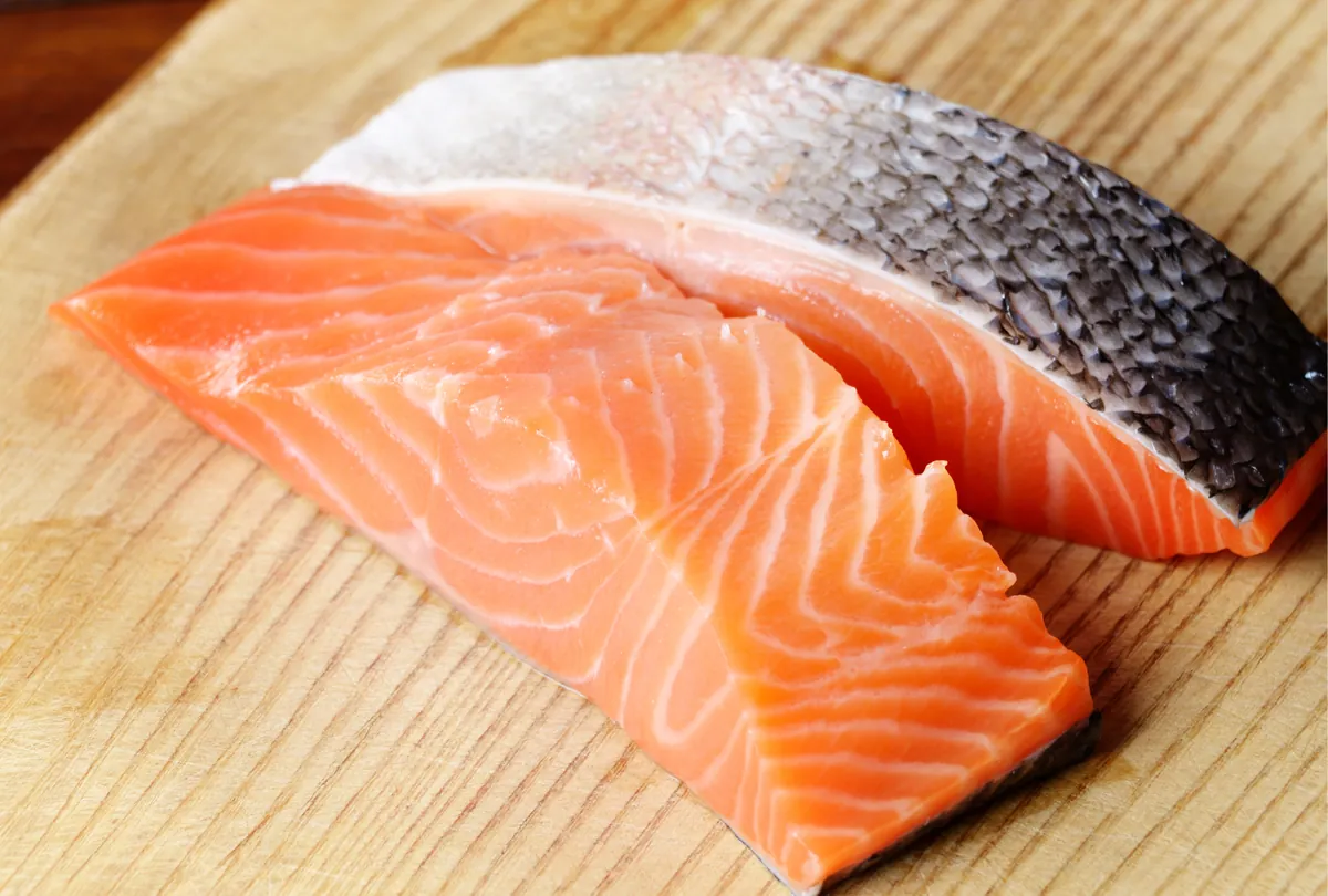 Fresh salmon fillet and raw salmon alongside raw chicken breast on a cutting board.
