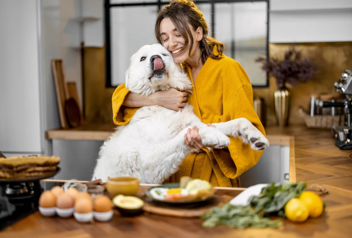 Woman in golden cardigan holding white dog with tongue out