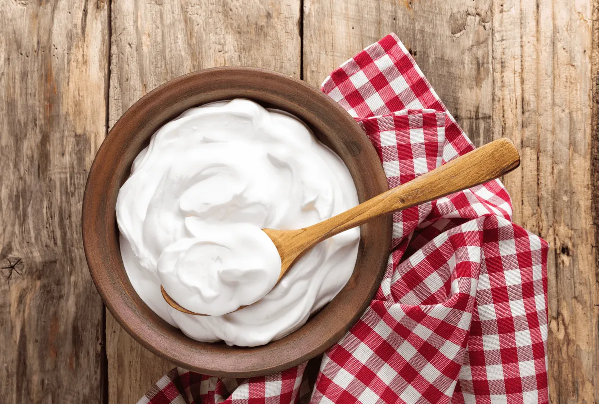 White yogurt in wooden bowl with spoon on red checkered cloth