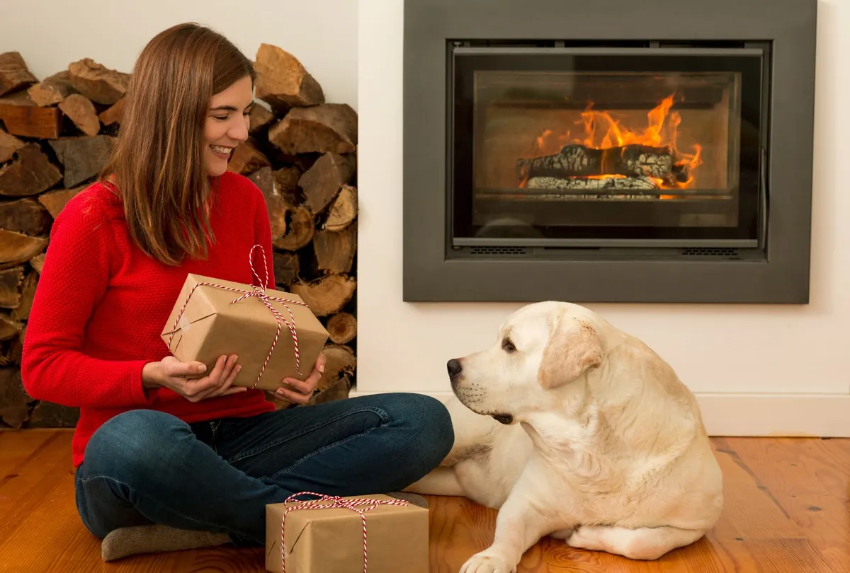 Woman in red sweater with yellow Labrador by fireplace